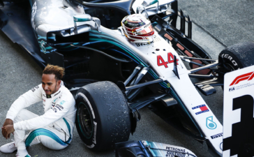 Lewis Hamilton sitting next to Formula 1 car