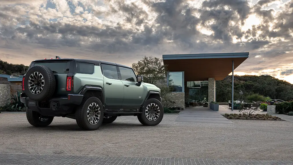 We see a grey-green 2024 Hummer EV SUV sitting in front of a fancy house somewhere. 