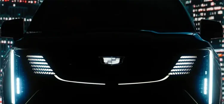 The front grill of a Cadillac Escalade IQ EV SUV is seen in darkness. The headlights are shining through.