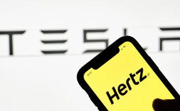 Hertz app running on an iPhone with Tesla logo in the background