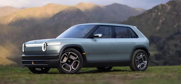 A silver Rivian R3 crossover electric utility vehicle is seen with its headlights on.