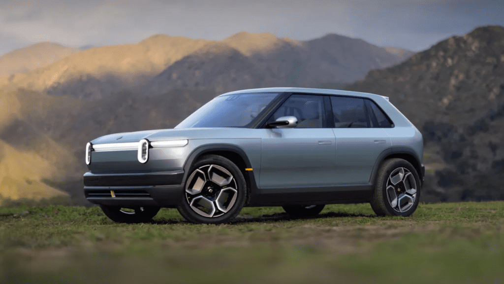Rivian R3 parked on a flat patch of land with a scenic mountainview background